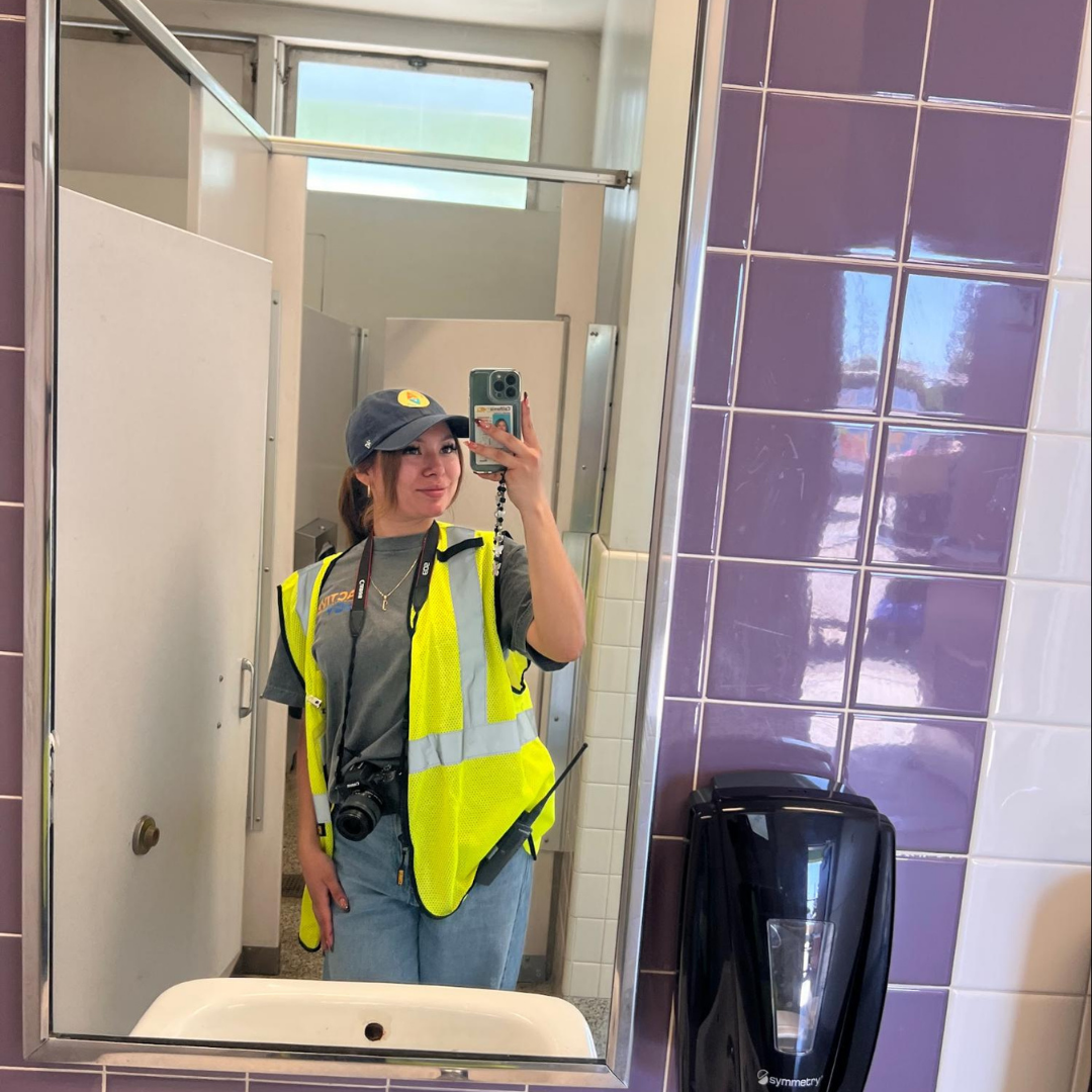 Jaylene wearing a safety vest, cap, camera, and radio.