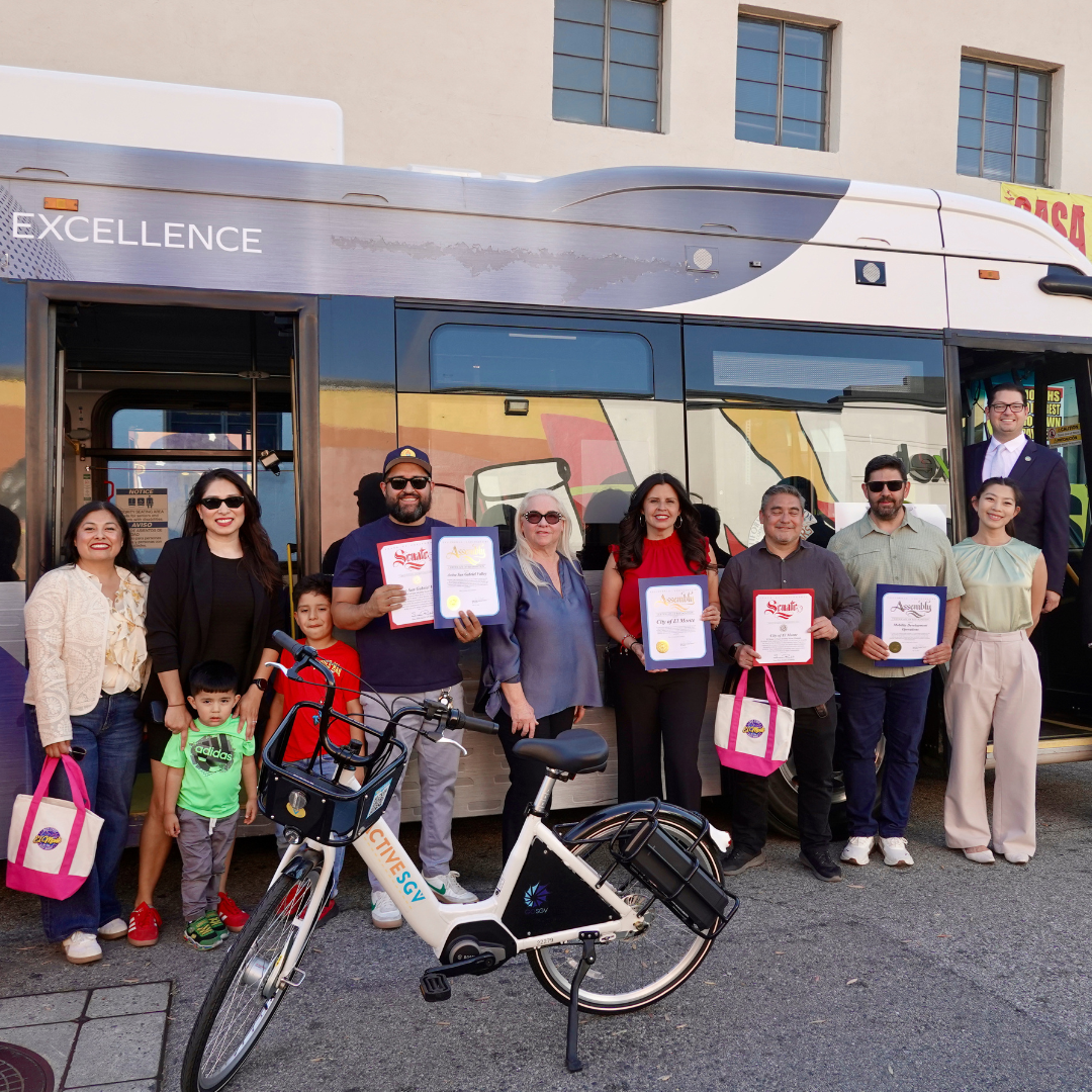 Community leaders and residents pose for a group photo beside an ActiveSGV e-bike and transit bus during a recognition event.