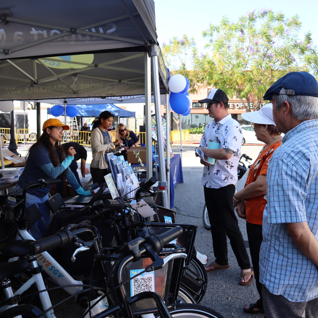 ActiveSGV staff speak with residents at an outdoor community event booth featuring e-bikes and mobility resources.