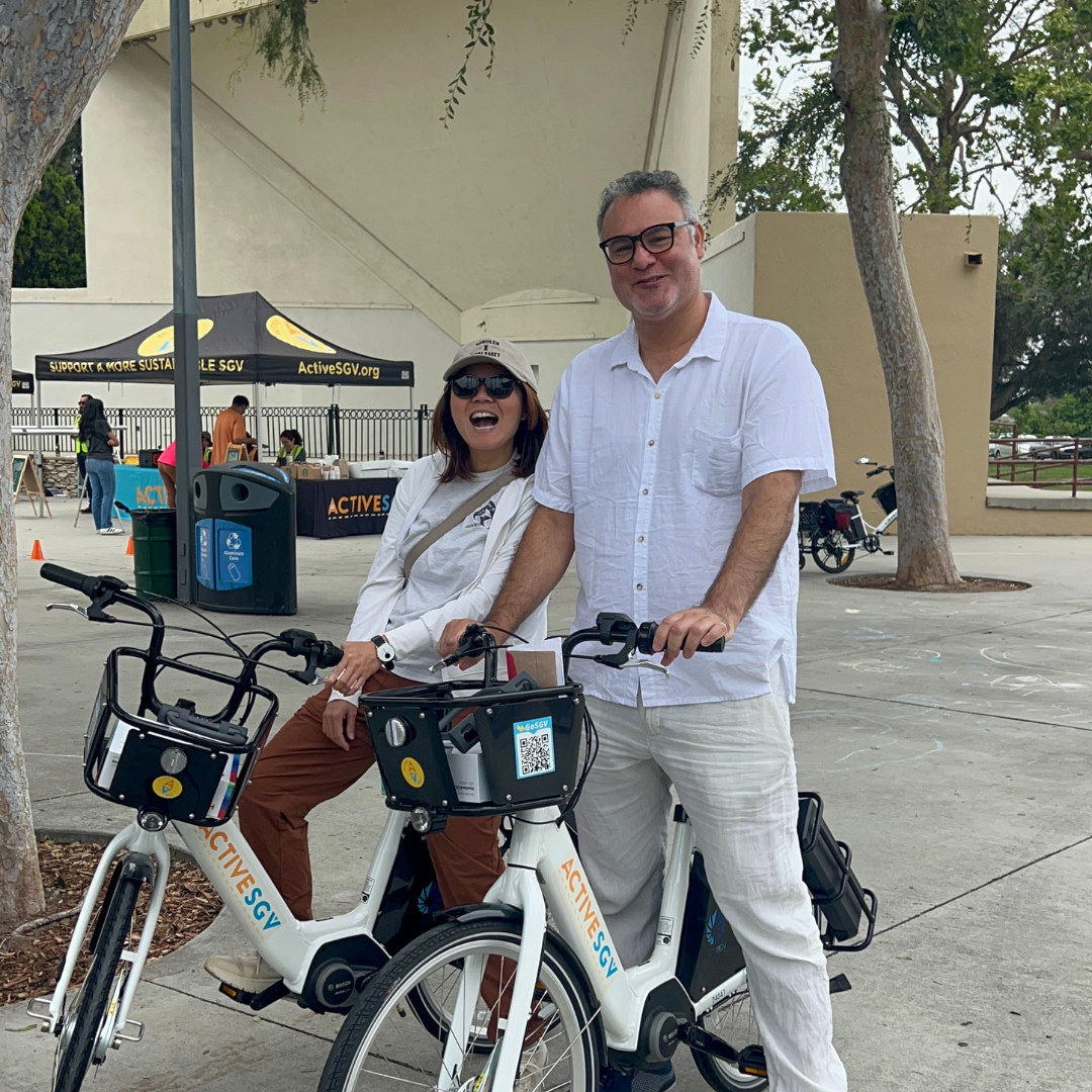 Two adults smile while posing with ActiveSGV e-bikes at a community event.