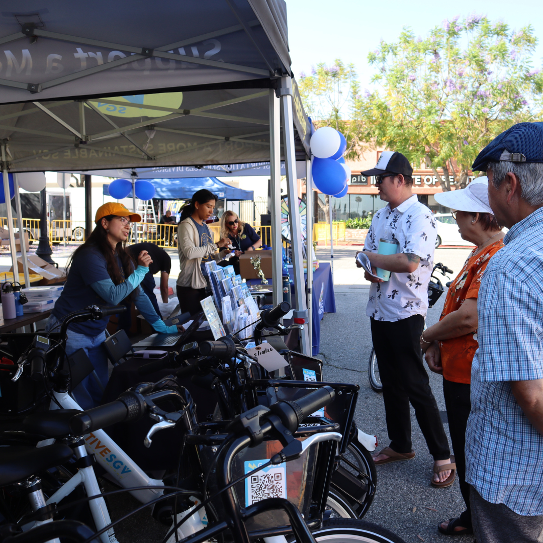 Staff members speak with visitors at an information booth displaying transportation resources and e-bikes.