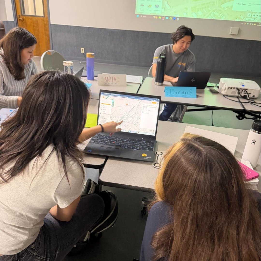 Participants gather around a laptop reviewing maps and data as part of a collaborative research activity during the Community Leadership Program.