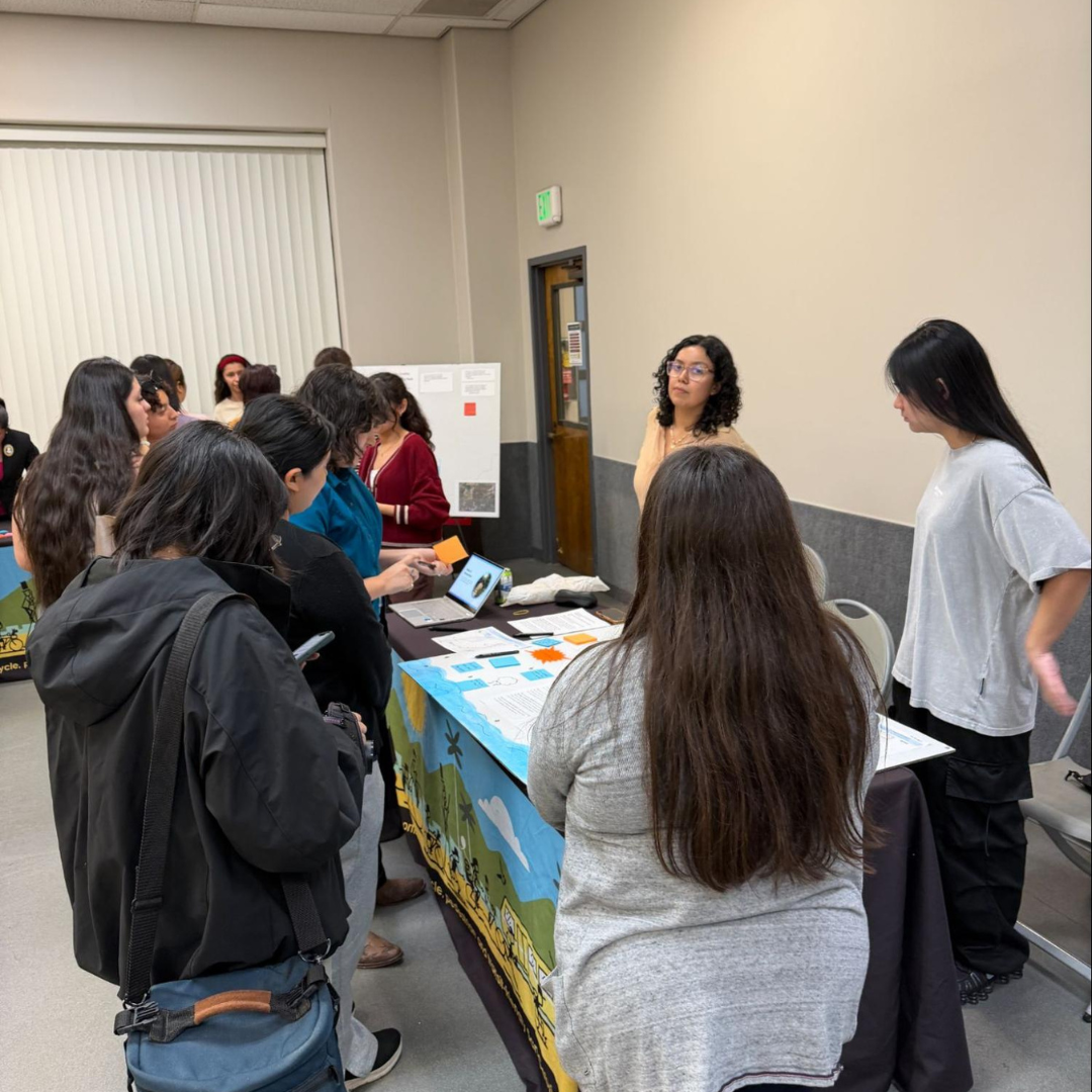 Community members gather around a project display table, reviewing materials and discussing environmental concerns with participants.