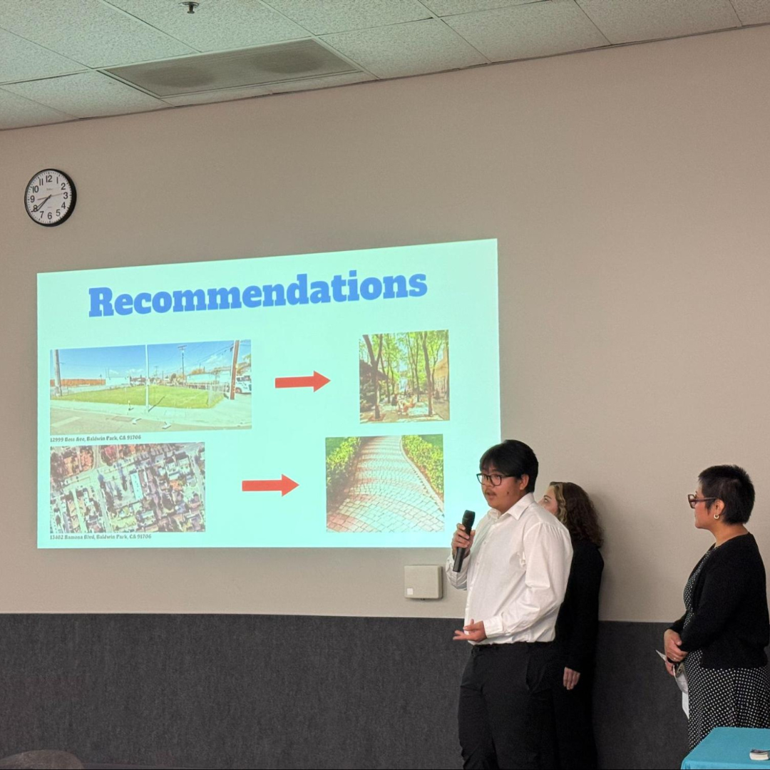 A participant presents recommendations for transforming underutilized paved areas into greener community spaces during a group presentation.