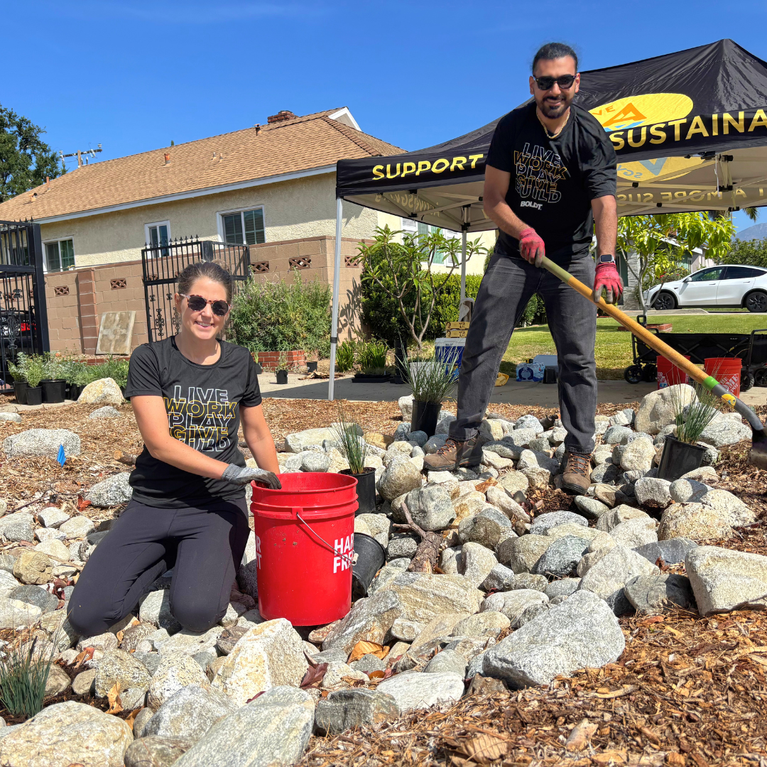 Two volunteers position large granite stones within a rain garden installation.