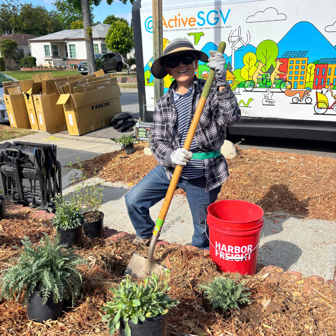Volunteer holding a shovel and smiling while standing in a newly planted rain garden.