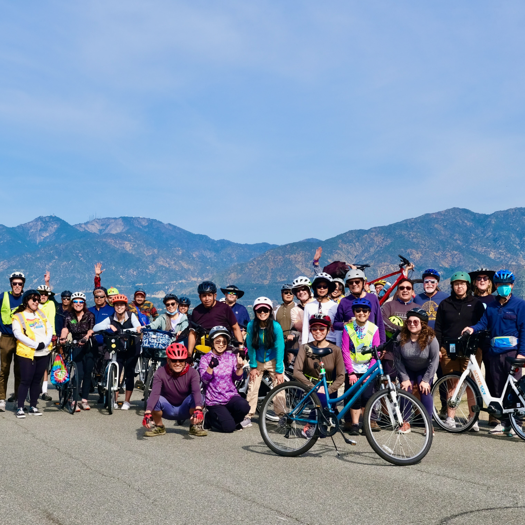 Large group of cyclists gathered for a community ride with mountains in the background.