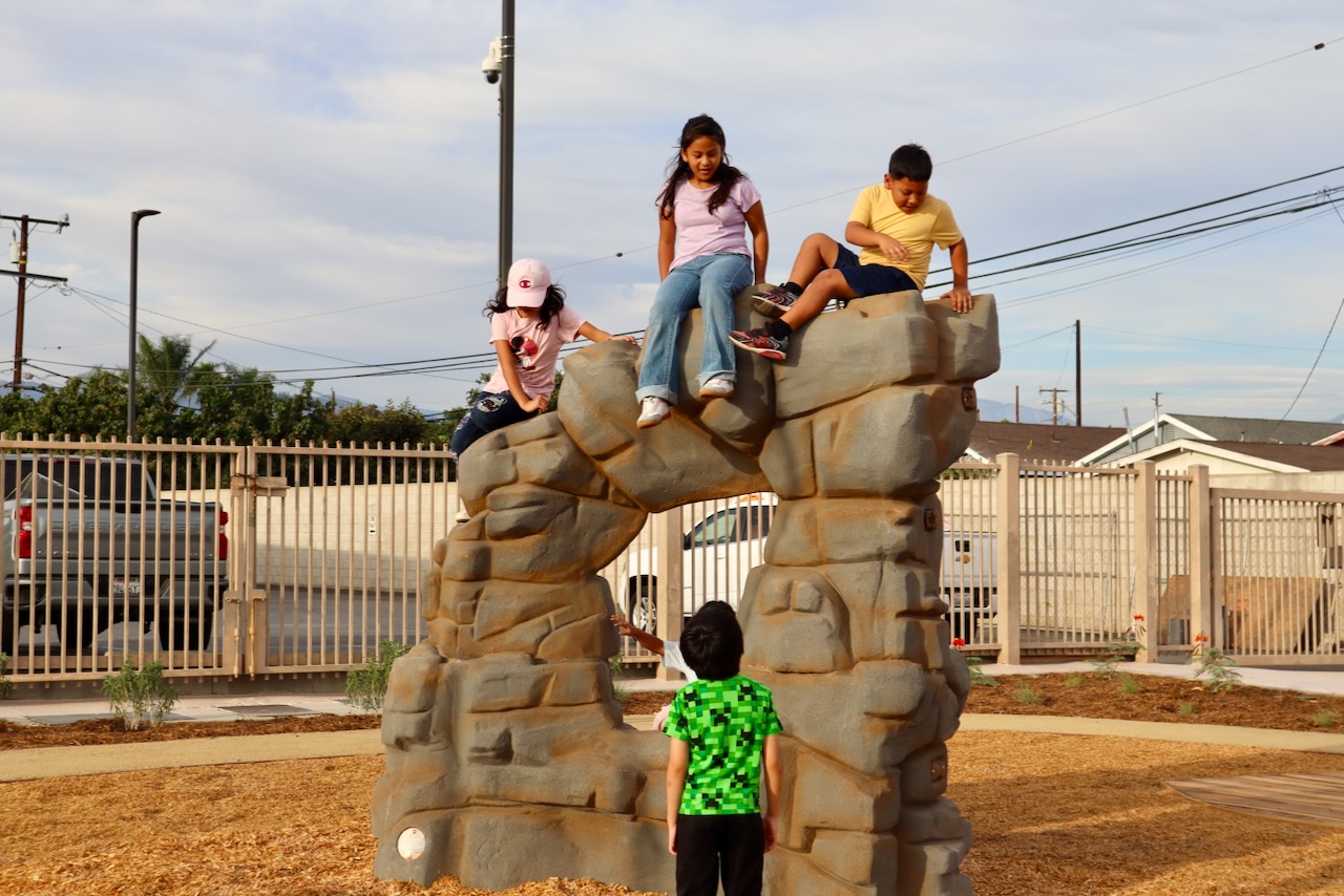 Four students climb and sit on top of a new boulder play structure in a mulched play area at Shirpser Elementary School.