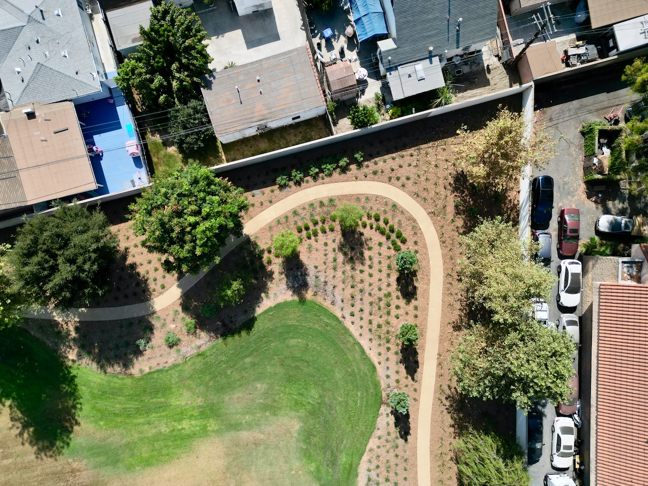 Aerial view of the new decomposed granite walking loop curving around the edge of a green play field, bordered by newly planted trees and shrubs.