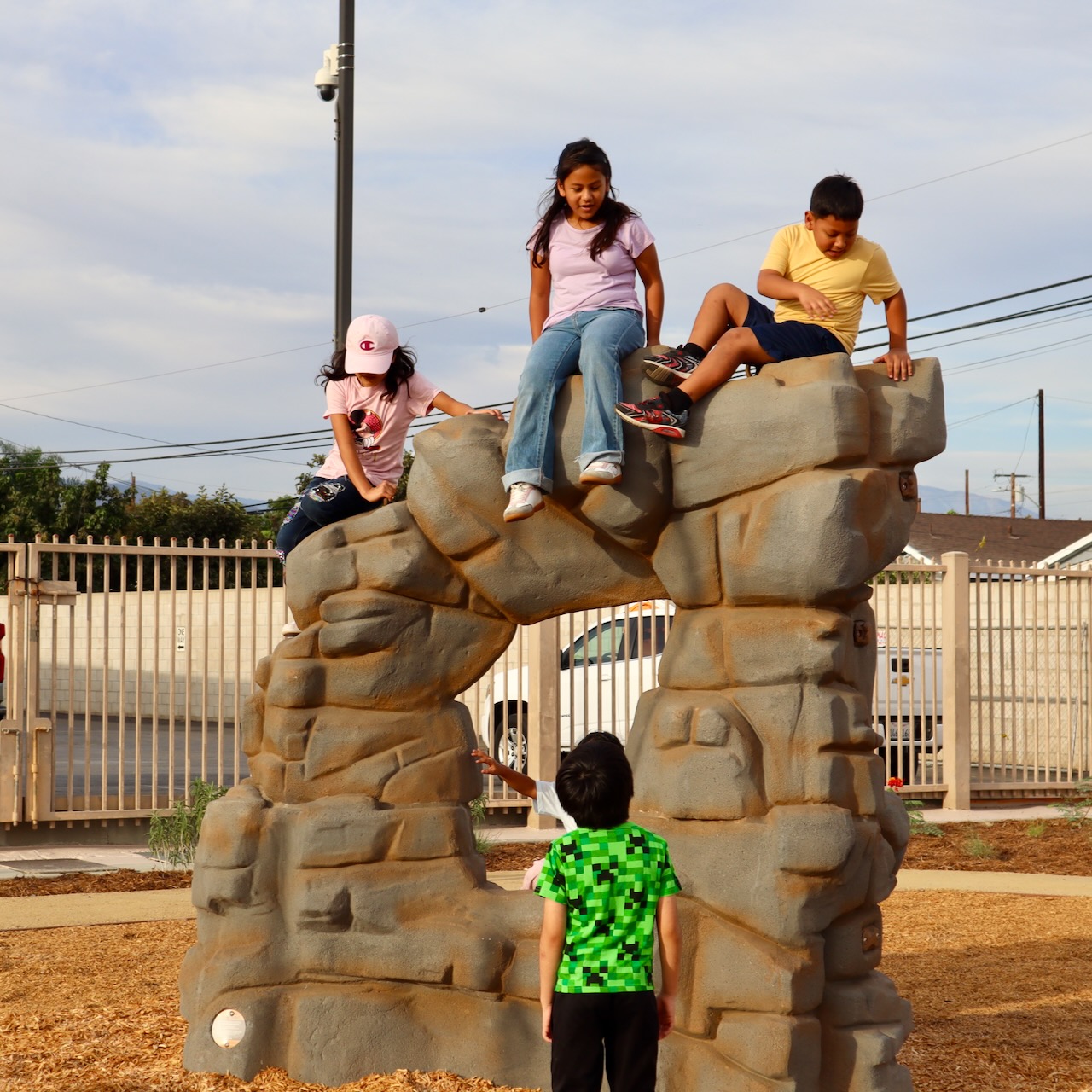Four students climb and sit on a new boulder play structure at Shirpser Elementary School.
