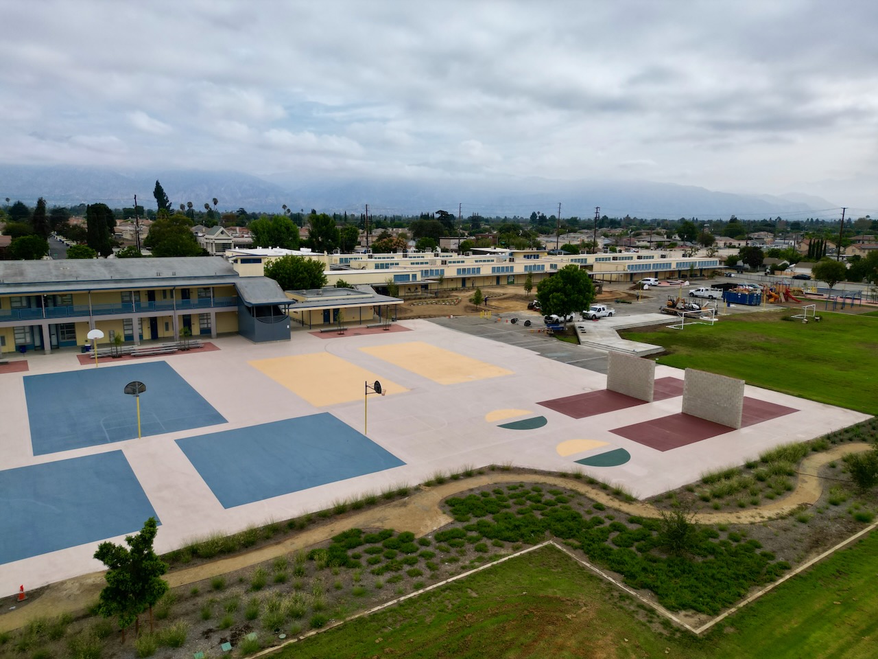 Aerial view of Gidley's resurfaced basketball and multi-use courts, handball walls, and new native planting, with the San Gabriel Mountains behind.