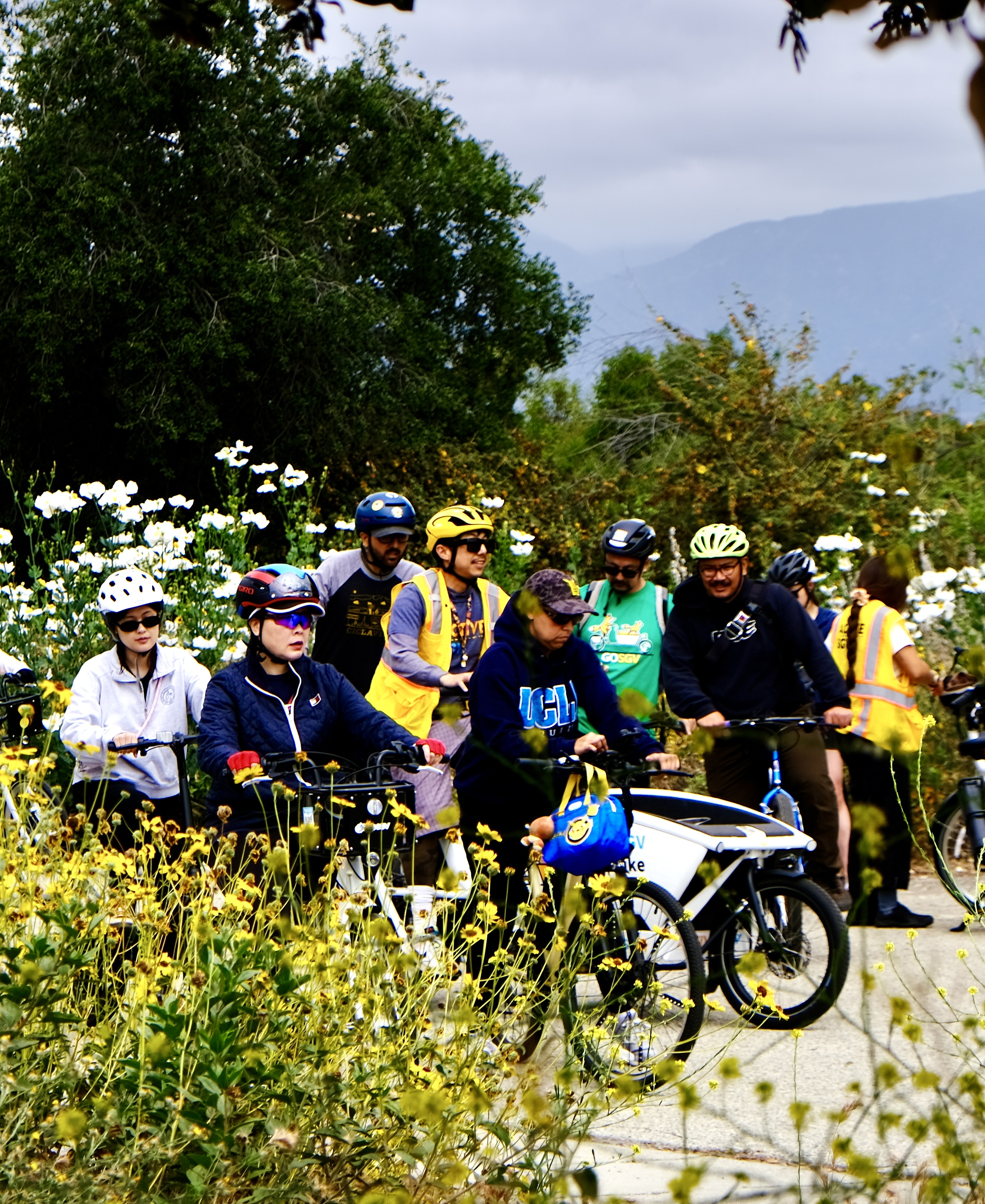 A person in a helmet riding an electric bike on a paved path at Santa Fe Dam Recreation Area, with the San Gabriel Mountains in the background.