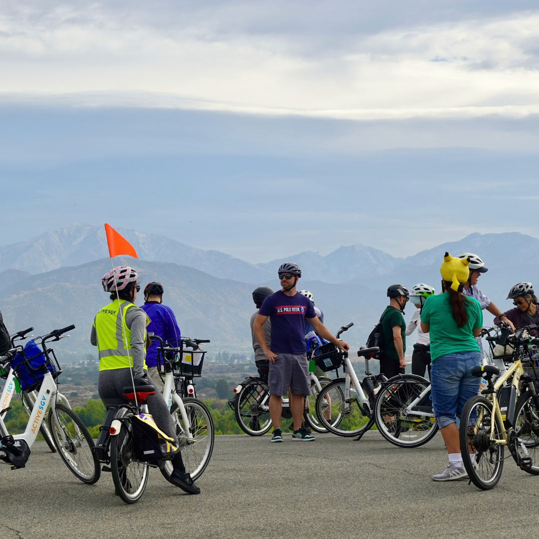 A group of cyclists gathered together. San Gabriel Mountains are visible in the background. 
