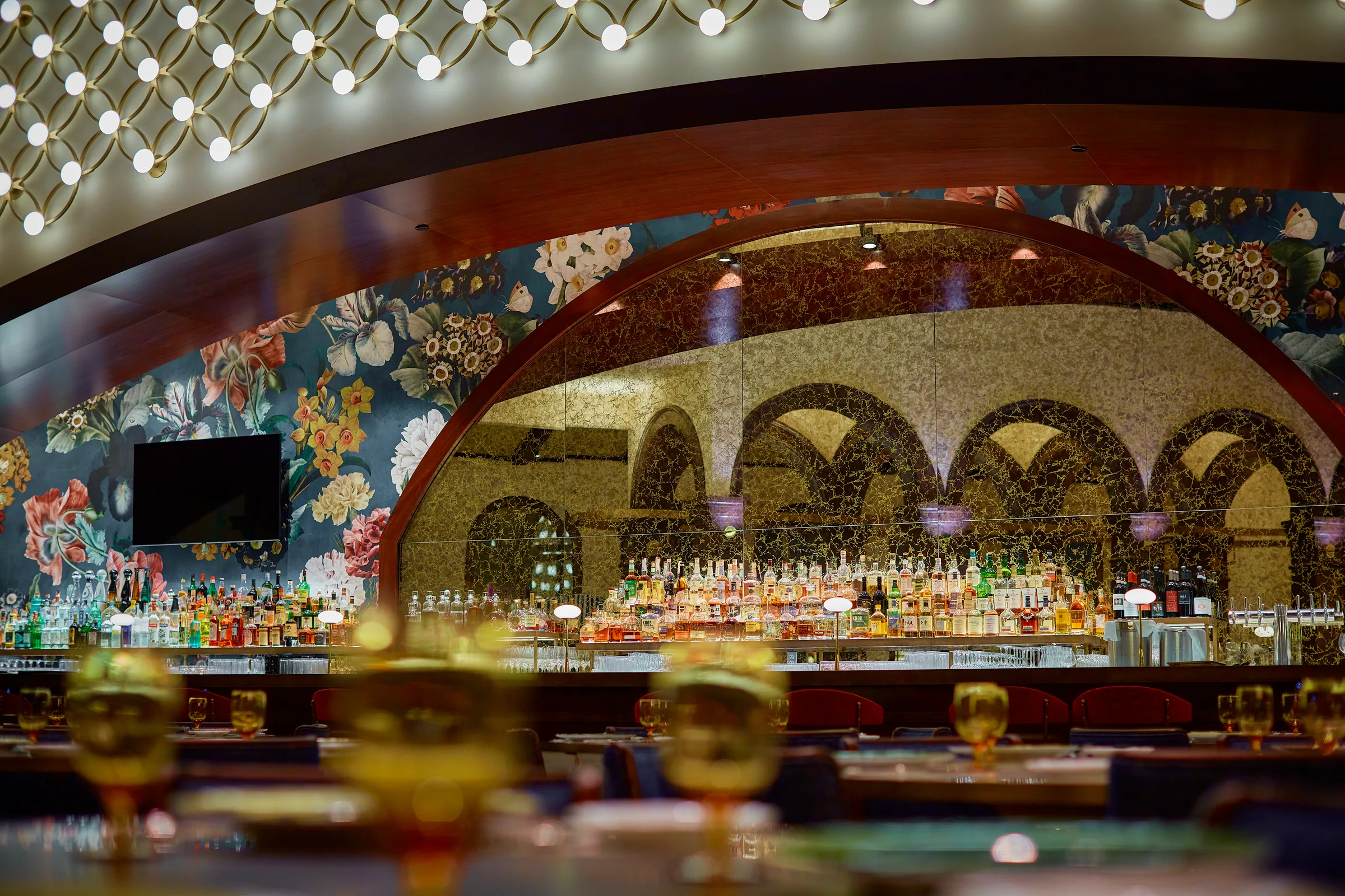 Carama back bar under an arched mural with floral wallpaper