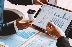 Two people analyzing financial charts and graphs on a laptop and printed paper during a business meeting.