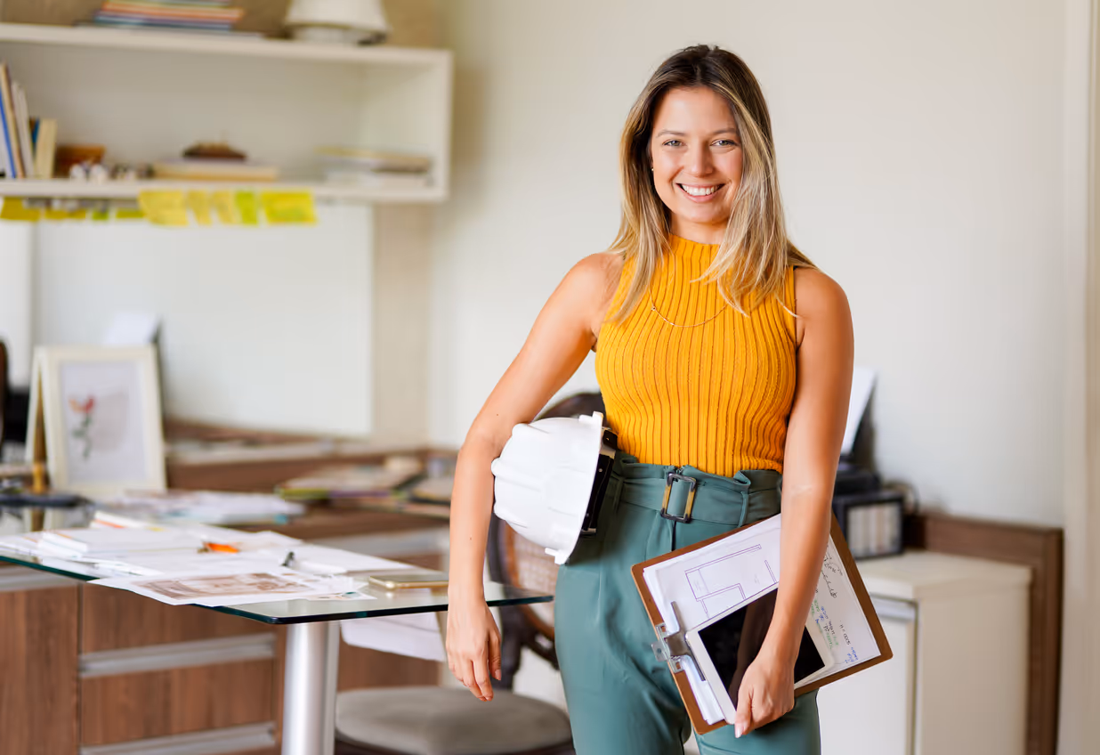 female engineer standing with a hardhat and clipboard in her office 