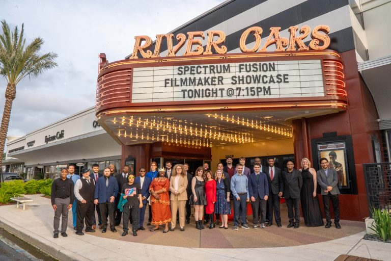 Group of people dressed in formal and semi-formal attire standing in front of the River Oaks theater marquee that reads: Spectrum Fusion Filmmaker Showcase Tonight @7:15PM.