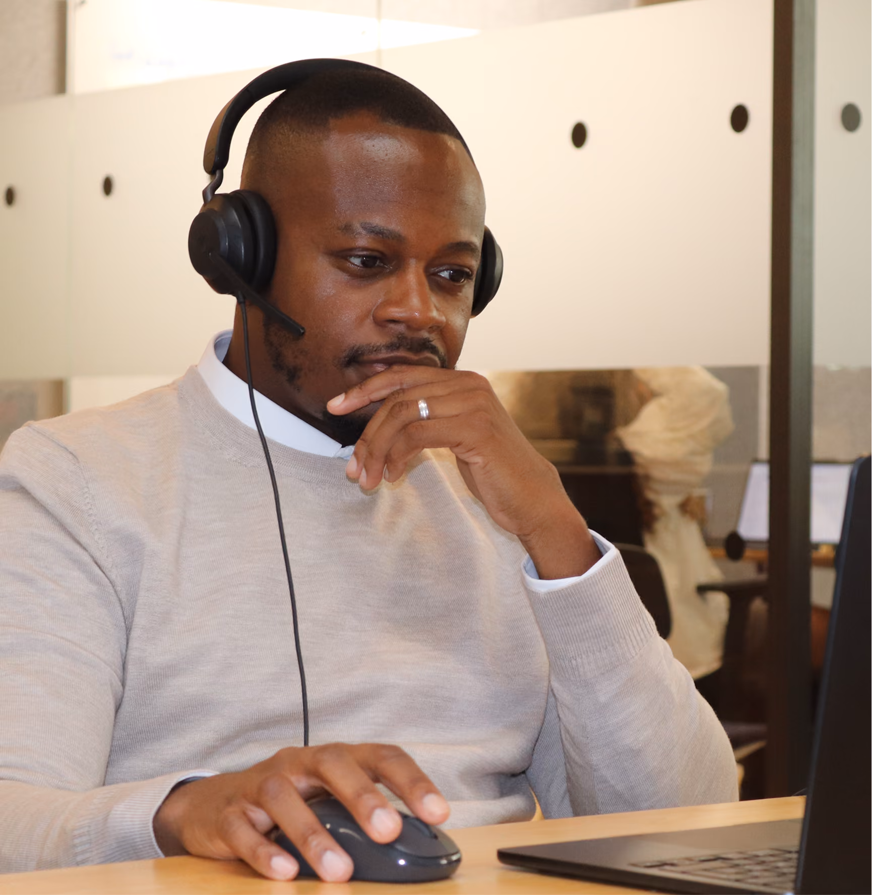 Homme portant un casque avec micro, assis devant un ordinateur portable, utilisant une souris et concentré sur l'écran.