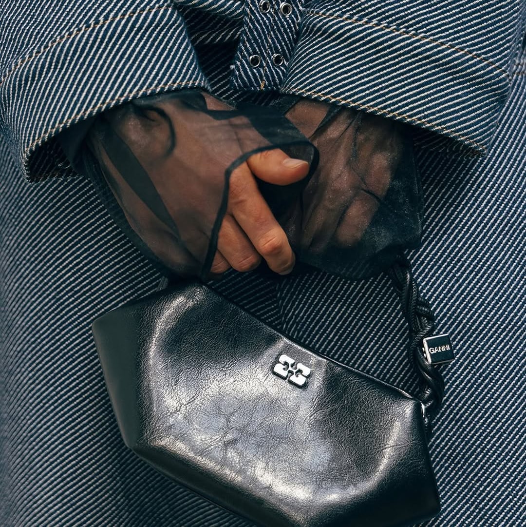 Close-up of hands holding a small black leather handbag over striped fabric.