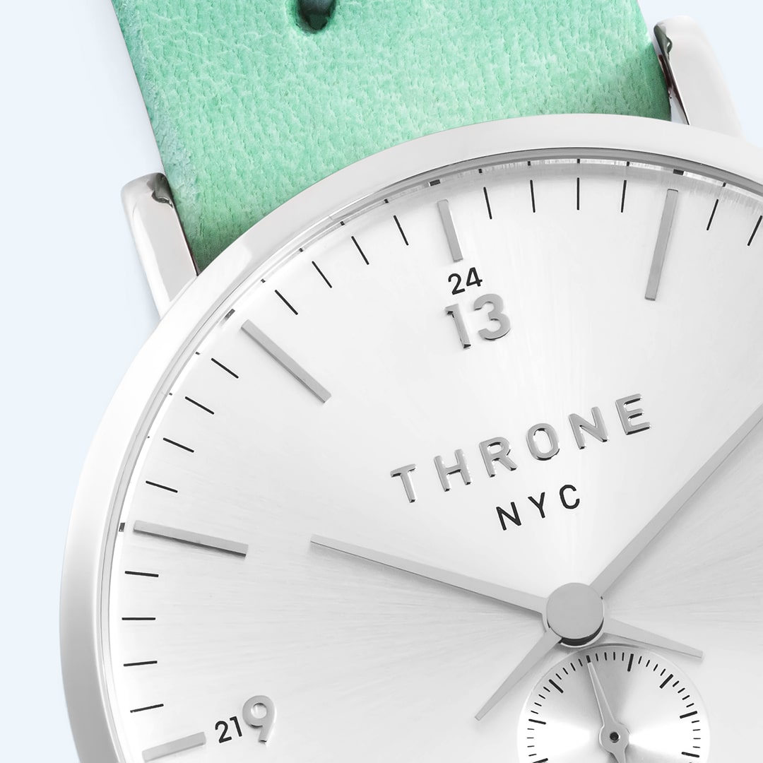 Close-up of a silver analog watch face with mint-green background elements.