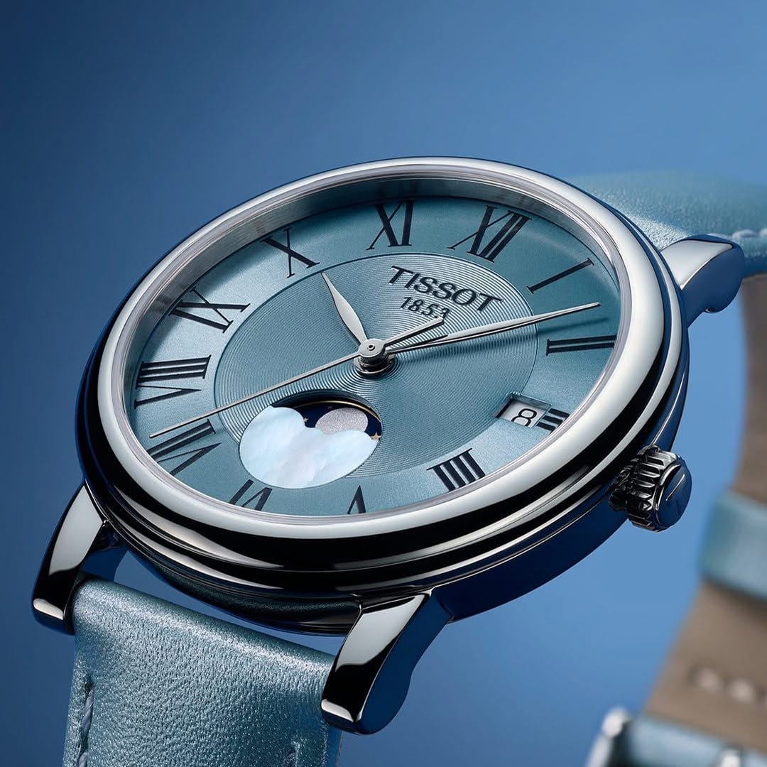 Close-up of the Tissot wristwatch with a blue dial and leather strap, photographed against a soft blue background.