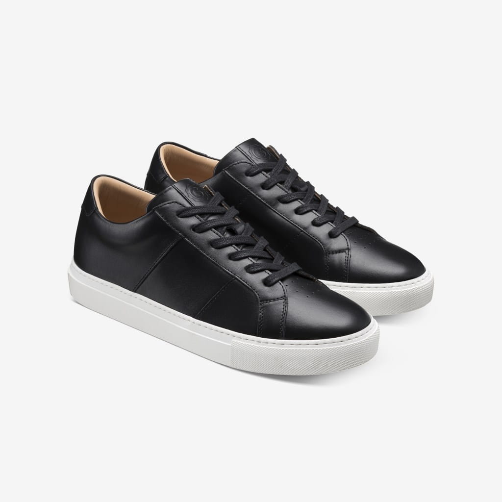 Pair of black leather sneakers with white soles on white background.