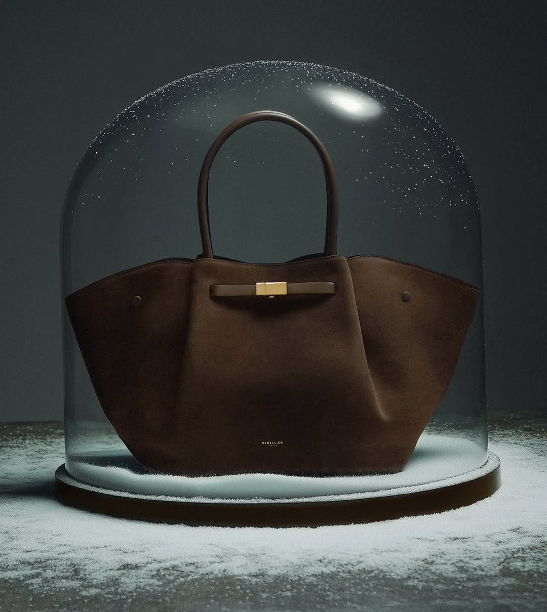 Brown leather tote bag displayed under a glass dome in dramatic lighting