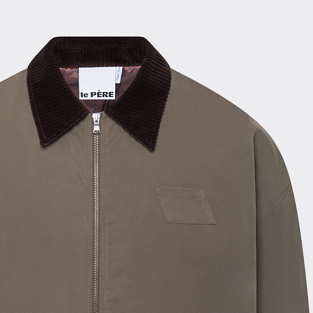 Le Pere olive zip jacket with dark brown corduroy collar and branded chest label, close-up detail shot on neutral background
