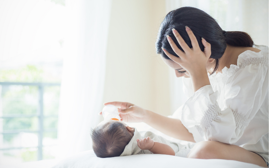 stressed mom holding her head while she bottle feeds baby