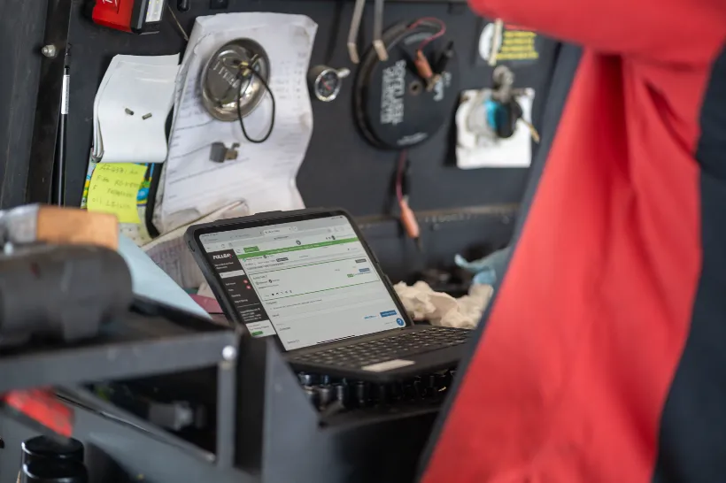 Laptop displaying diagnostic software for a truck's electrical systems beside wiring tools and service notes in a truck shop.