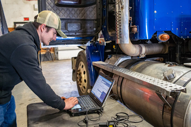 SCR diagnostics on a heavy-duty truck with technician using laptop for emissions system troubleshooting.