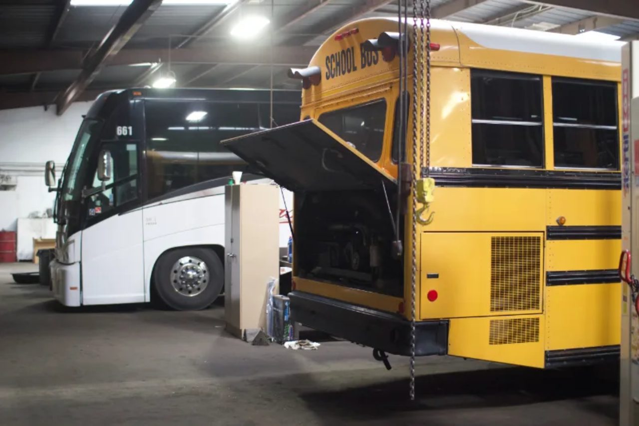 Fall bus maintenance in Chicago, with a yellow school bus's engine compartment open beside a white coach bus in a repair shop.
