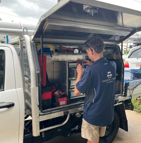 A Tropical Coast Plumbing technician works at the back of a service vehicle, organising tools and equipment from the open storage compartment.