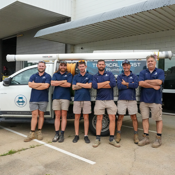 Members from Tropical Coast Plumbing stand smiling in front of a branded work vehicle parked outside their office.