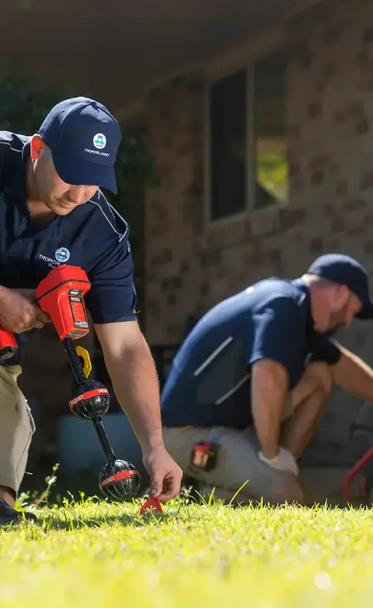 Two Tropical Coast Plumbing technicians performing a CCTV drain inspection outside a home, using specialised camera and diagnostic equipment to locate and assess pipe blockages.