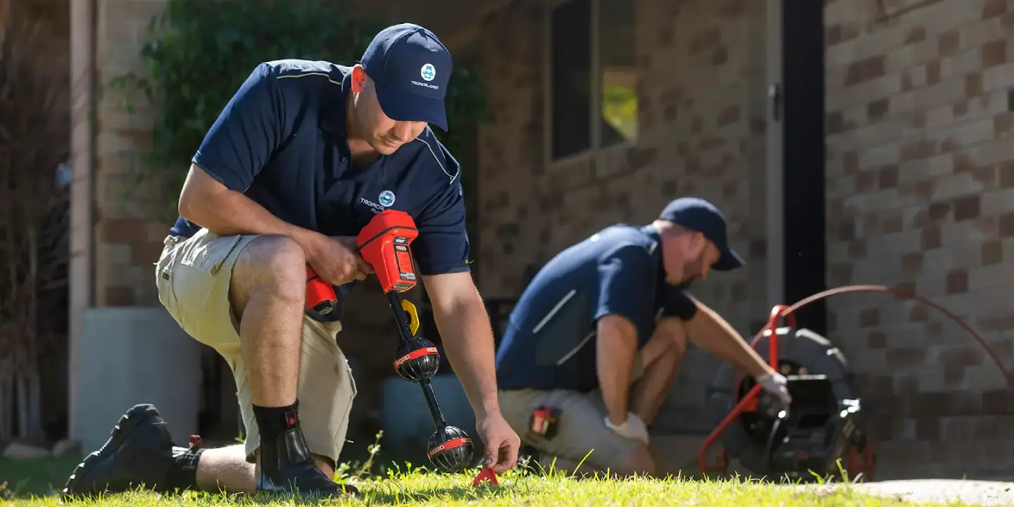 Plumber using pipe locator while another clears drain during emergency plumbing callout.