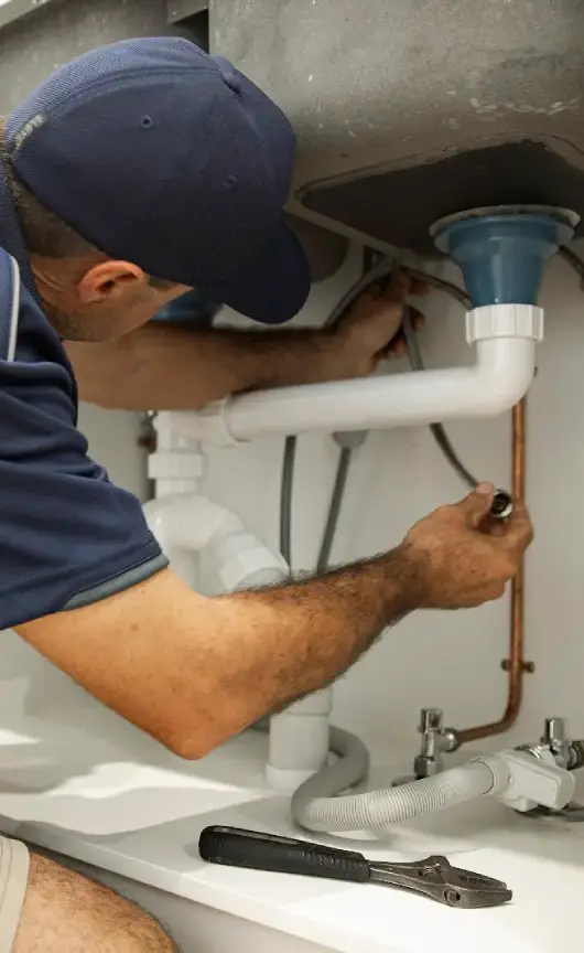 Technician tightening fittings on a kitchen drainage pipe as part of emergency leak repair