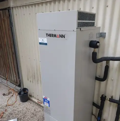 Outdoor Thermann gas hot water system installed against a corrugated metal wall.