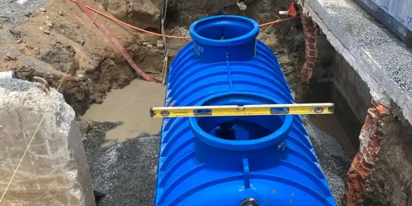 Installation of a large blue commercial grease trap tank at a construction site, showing professional plumbing setup for effective wastewater management.