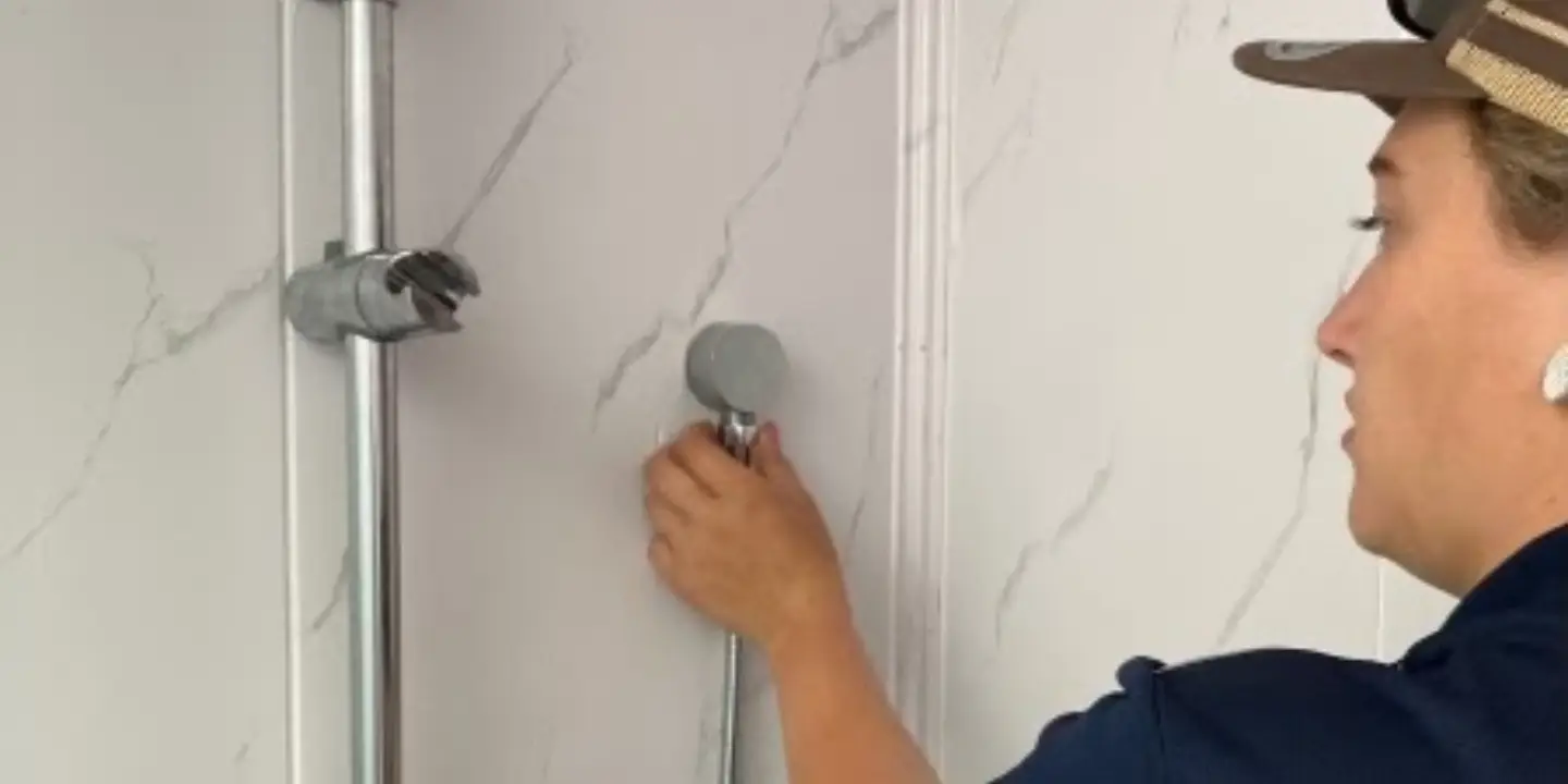 Tropical Coast Plumbing technician adjusting a handheld showerhead inside a tiled bathroom.