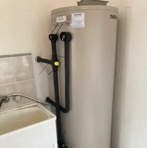 Installed electric hot water storage system connected to household plumbing beside a laundry sink, providing a reliable hot water supply.