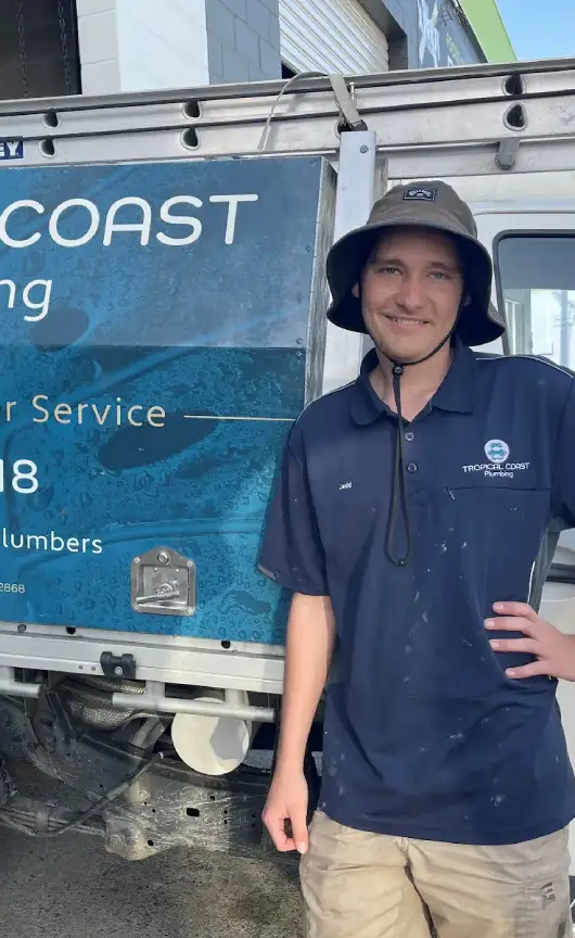 A Tropical Coast Plumbing worker smiling beside a company vehicle.