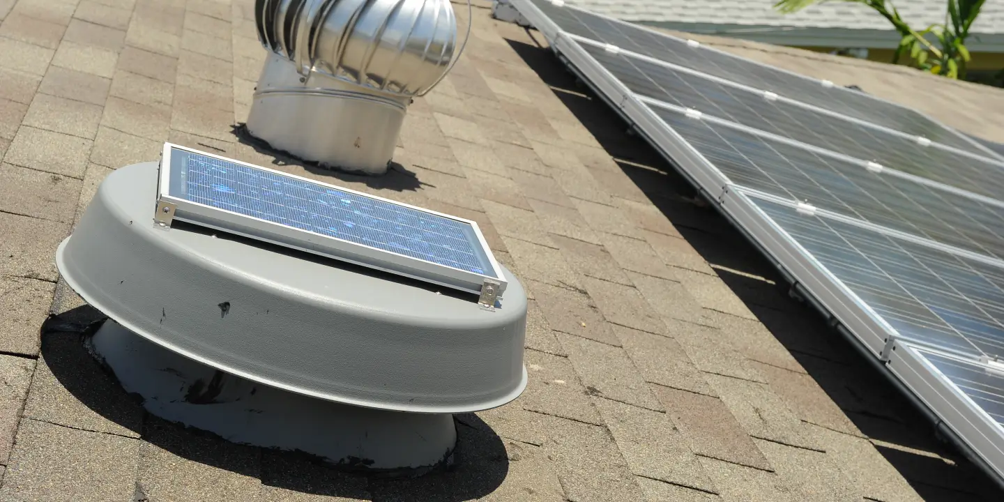 Technician installing a Solar King fan unit on a metal roof, surrounded by tools and safety gear during a solar ventilation setup.