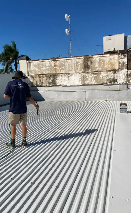 A worker from Tropical Coast Plumbing hosing down a freshly treated roof surface as part of a solar installation preparation or maintenance procedure.