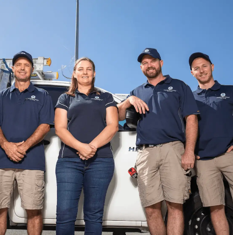 Members from Tropical Coast Plumbing stand smiling in front of a branded work vehicle parked outside their office.