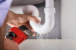 Emergency plumber tightening a leaking P-trap under a kitchen sink with a wrench, water leak repair during a call-out in Yeppoon.