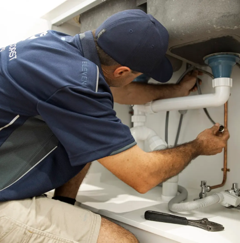 Plumber working under a sink on PVC waste pipes, diagnosing a blocked drain and completing an emergency repair in a Yeppoon home.