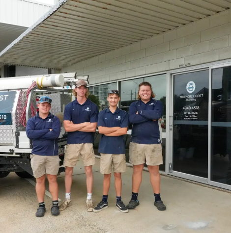 Members from Tropical Coast Plumbing stand smiling in front of a branded work vehicle parked outside their office.