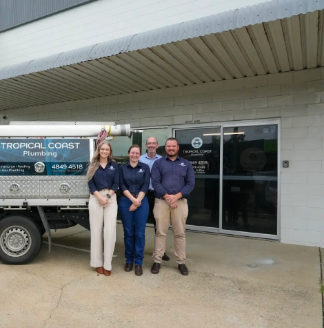 Members from Tropical Coast Plumbing stand smiling in front of a branded work vehicle parked outside their office.