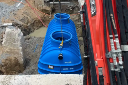Excavator lowering a large blue grease trap into the ground during plumbing installation work in Central Queensland.